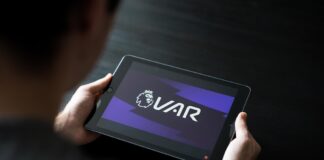 a person can be seen looking at VAR on their tablet during a football match