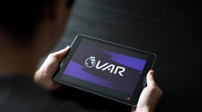 a person can be seen looking at VAR on their tablet during a football match