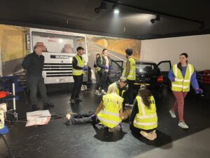 2 students perform first aid on a test-dummy whilst 3 others search vehicles for evidence