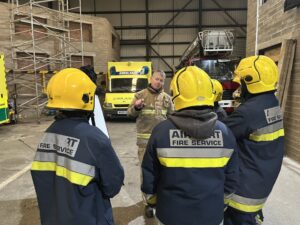 Fire instructor briefs 3 students in turnout gear before fire-fighting exercise.