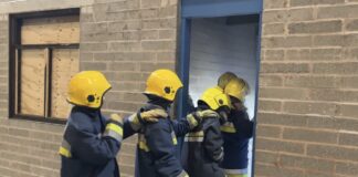 4 policing students in turnout overalls enter a derelict training building lit by torchlight