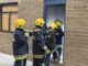 4 policing students in turnout overalls enter a derelict training building lit by torchlight