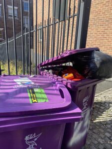 Two overflowing purple bins outside a building in Liverpool. Photo copyright - Hannah O'Sullivan (BA Journalism 2025)