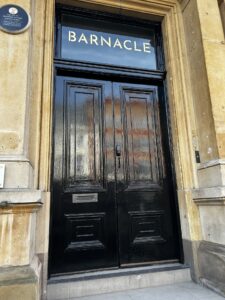The image shows the black front door of the restaurant with Barnacle across the top in gold lettering.