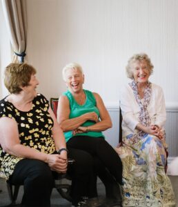 Image shows group of women sat down smiling, all appear joyful and laughing. 