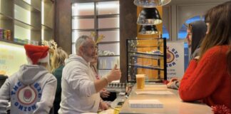 An image of Chris Lewis and other Big Onion staffers chatting with customers while serving beer at the community hub, with a display of baked goods in the background.