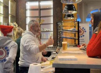 An image of Chris Lewis and other Big Onion staffers chatting with customers while serving beer at the community hub, with a display of baked goods in the background.