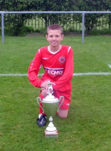Image of Oliver King, boy who suffered cardiac arrest aged 12, posed behind trophy