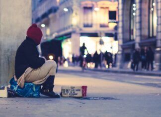 A Homeless person on the street wrapped in a blanket asking for money.