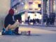 A Homeless person on the street wrapped in a blanket asking for money.