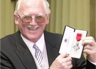 An image of Bill Tidy smiling as he receives his MBE