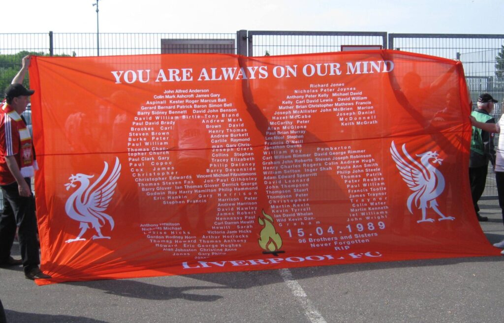 An image of fans holding a banner commemorating the 96 fans that lost thier lives, on the 20th anniversary of the disaster.