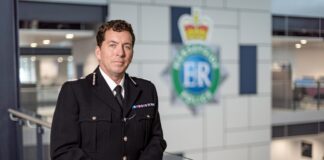 Chief Constable of Merseyside Police at the headquarters, leaning against a railing with the Merseyside police badge blurred behind. (c) Merseyside Police