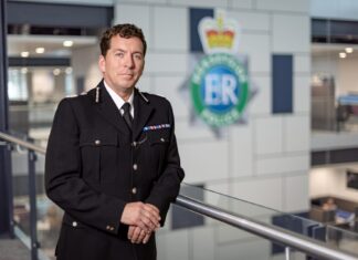 Chief Constable of Merseyside Police at the headquarters, leaning against a railing with the Merseyside police badge blurred behind. (c) Merseyside Police