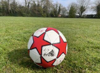 This photo shows a football sitting on short green grass in an open field. The ball is white with big red star shapes and looks a bit scuffed and used.