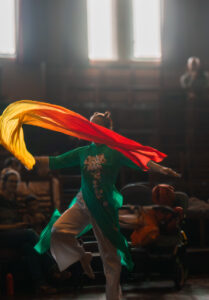 Female dancer in the blue attire dancing with a red and yellow ribbon.
