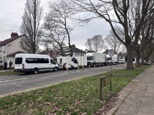 A series of white vans and lorries, parked along a residential street.