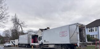 Two white lorries filled with filming equipment parked at the side of a residential street.