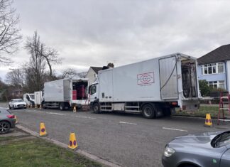 Two white lorries filled with filming equipment parked at the side of a residential street.