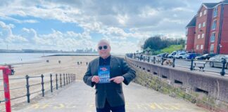 Paul Chase stands on the entrance to a beach holding a copy of his book 'Chelsea Nights'