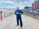 Paul Chase stands on the entrance to a beach holding a copy of his book 'Chelsea Nights'